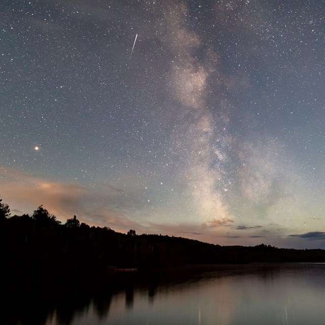 a starry night sky with the milky way and a shooting star over calm water