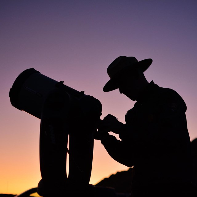 a silhouette of a ranger looking through a telescope at dusk