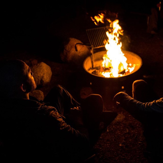 two people sit next to a campfire at night