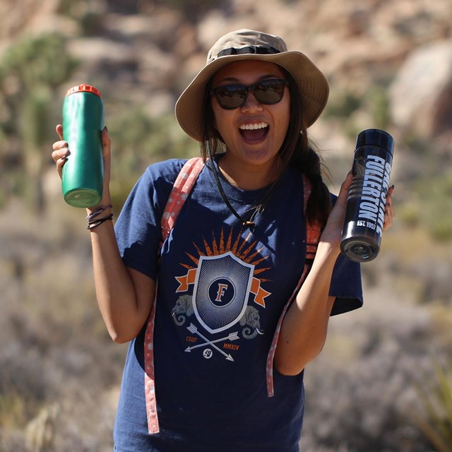 a smiling woman in a hat holds up two water bottles