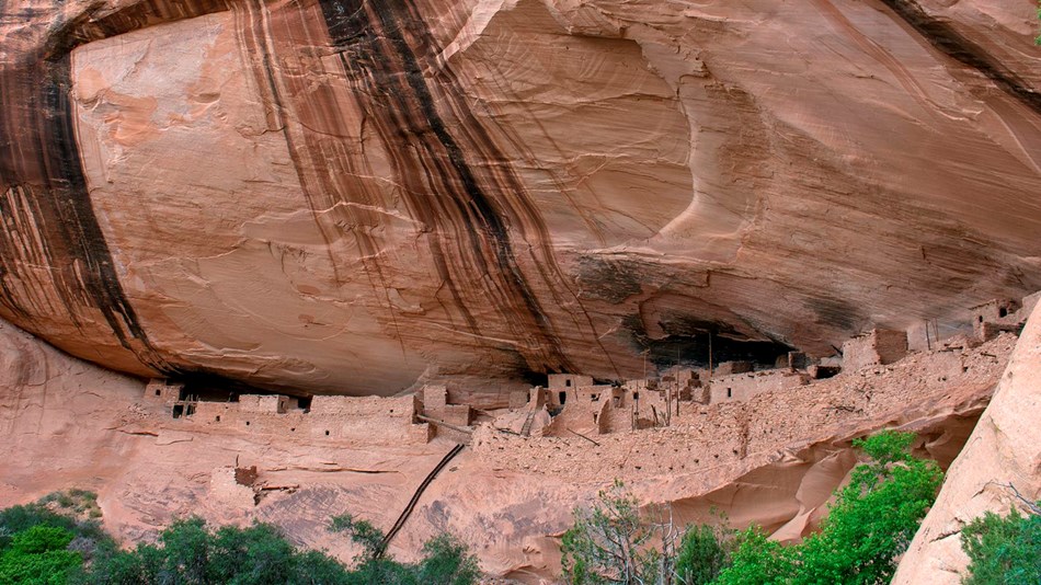 Houses made of sandstone, mud mortar, and wood are sheltered in a cliff alcove. 