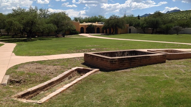 three rectangular brick structures aligned in a row, visitor center in background