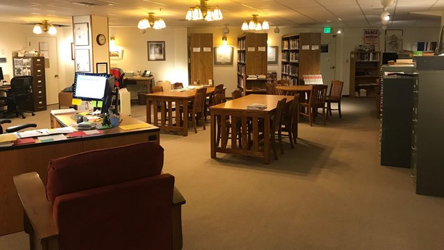 A room with many tables, chairs, books, and bookshelves sits empty.