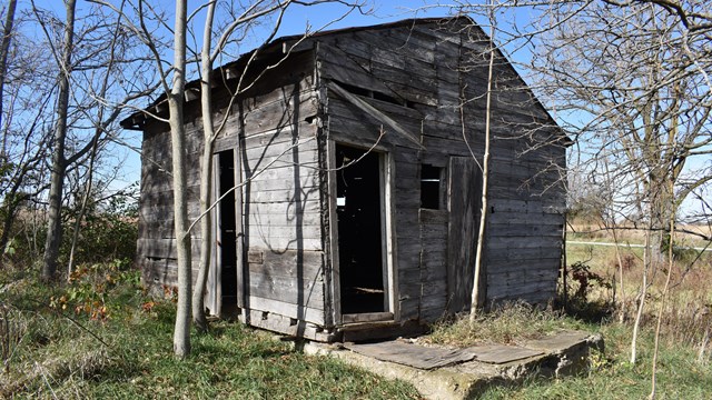 A wooden cabin with holes in its walls and broken pieces of wood hanging over the door.