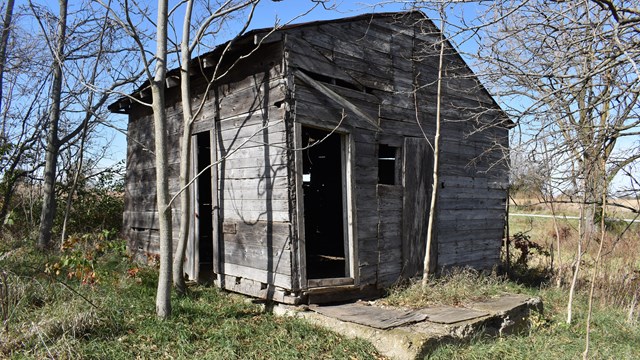 A wooden cabin with holes in its walls and broken pieces of wood hanging over the door.