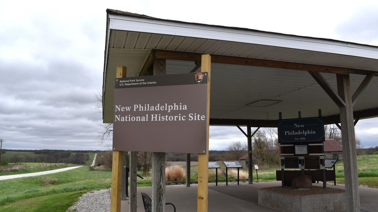 A New Philadelphia National Historic Site sign stands in front of an open-sided information kiosk.