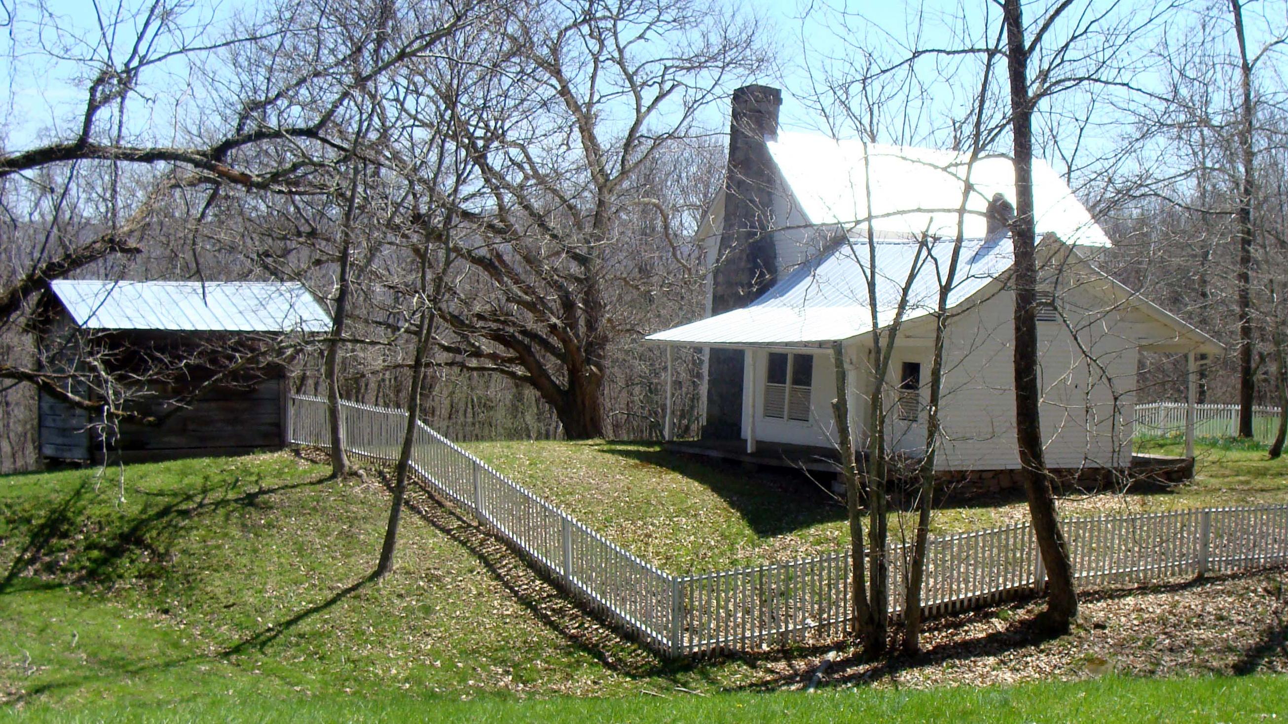 A white house surrounded by a simple wood fence in a grassy field with a few trees