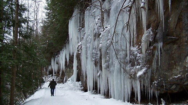 hiker walking alongside frozen waterfall