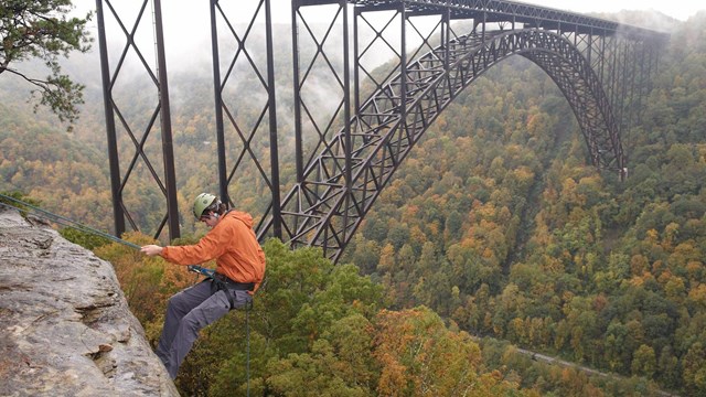 rock climber rappelling off cliff with bridge in background