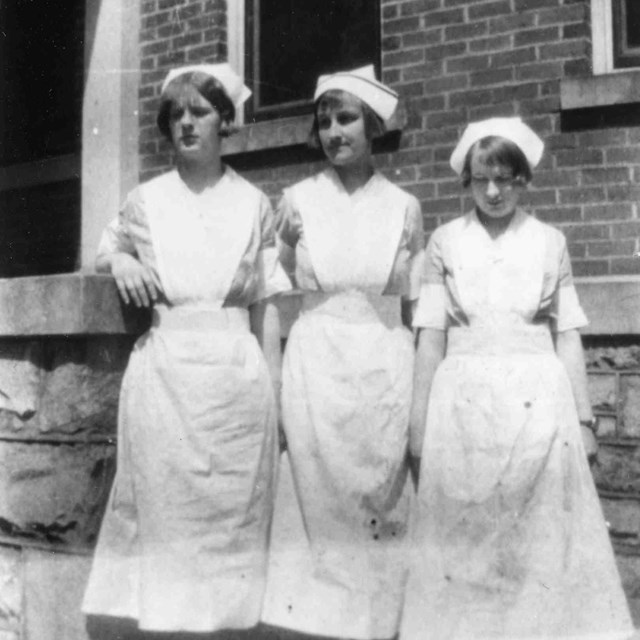 Historic photo of three nurses in front of a brick hospital 