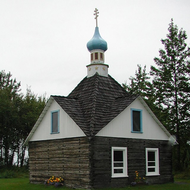 A Russian Orthodox chapel with log walls and blue and white roof with dome.