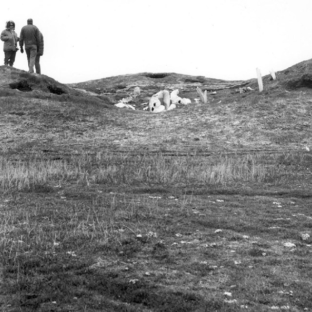 Historic photo of people standing on archaeological mounds with whale bone structure ruins.