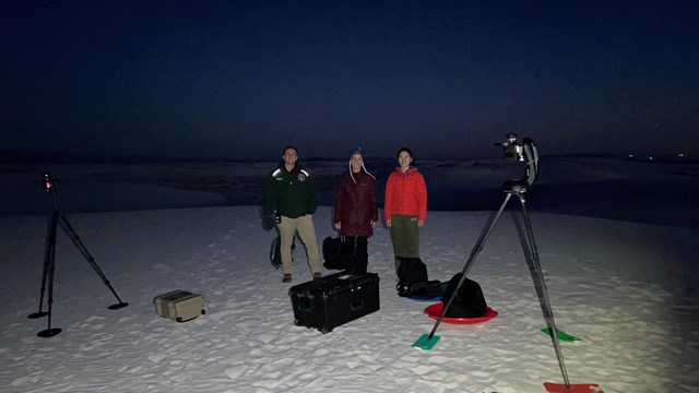 three researchers stand next to equipment for measuring night sky brightness