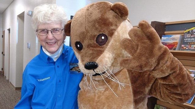 Volunteer standing with River Otter mascot. 