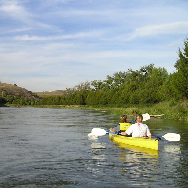 Two kayakers in a yellow boat on a calm river.