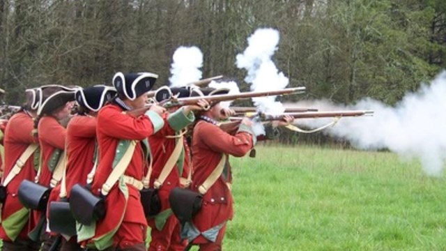 Two lines of soldiers in red coats fire muskets with smoke coming out of them.