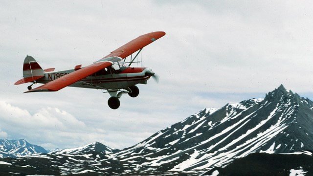 a red and white plane flies above mountains during spring