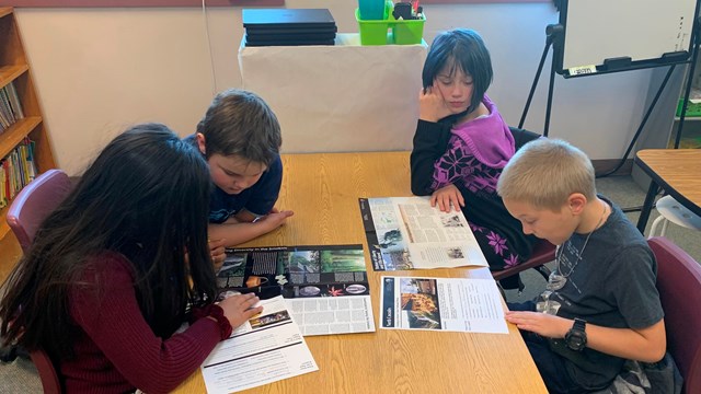 Four students sitting at a desk with maps in front of them