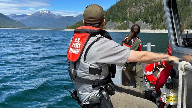 Park Ranger sitting on the side of the boat looking towards the lake and mountain in the distance