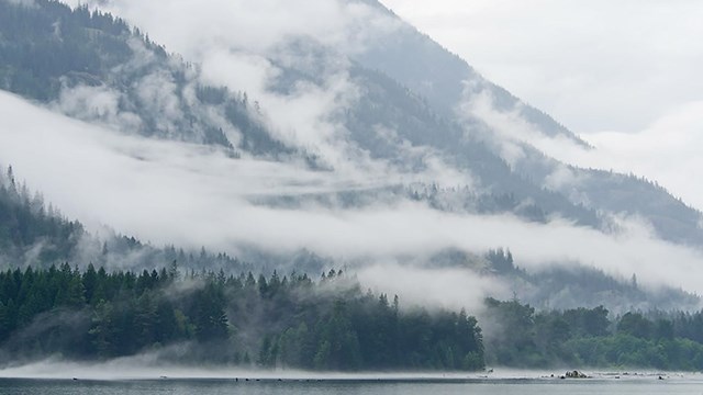 Clouds hang low over the lake, trees and mountainscape. 