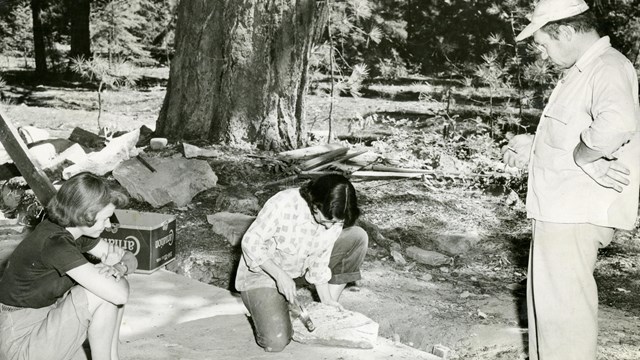 Three people work on a concrete foundation with tools around.