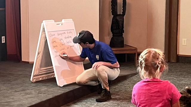 man writing on a board with a child in the foreground 