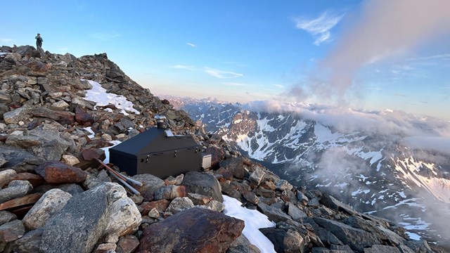 a rocky mountain top with a pit toilet. 