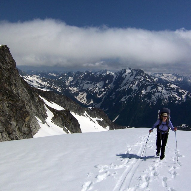 A climber crosses a snow field with mountains in the distance.