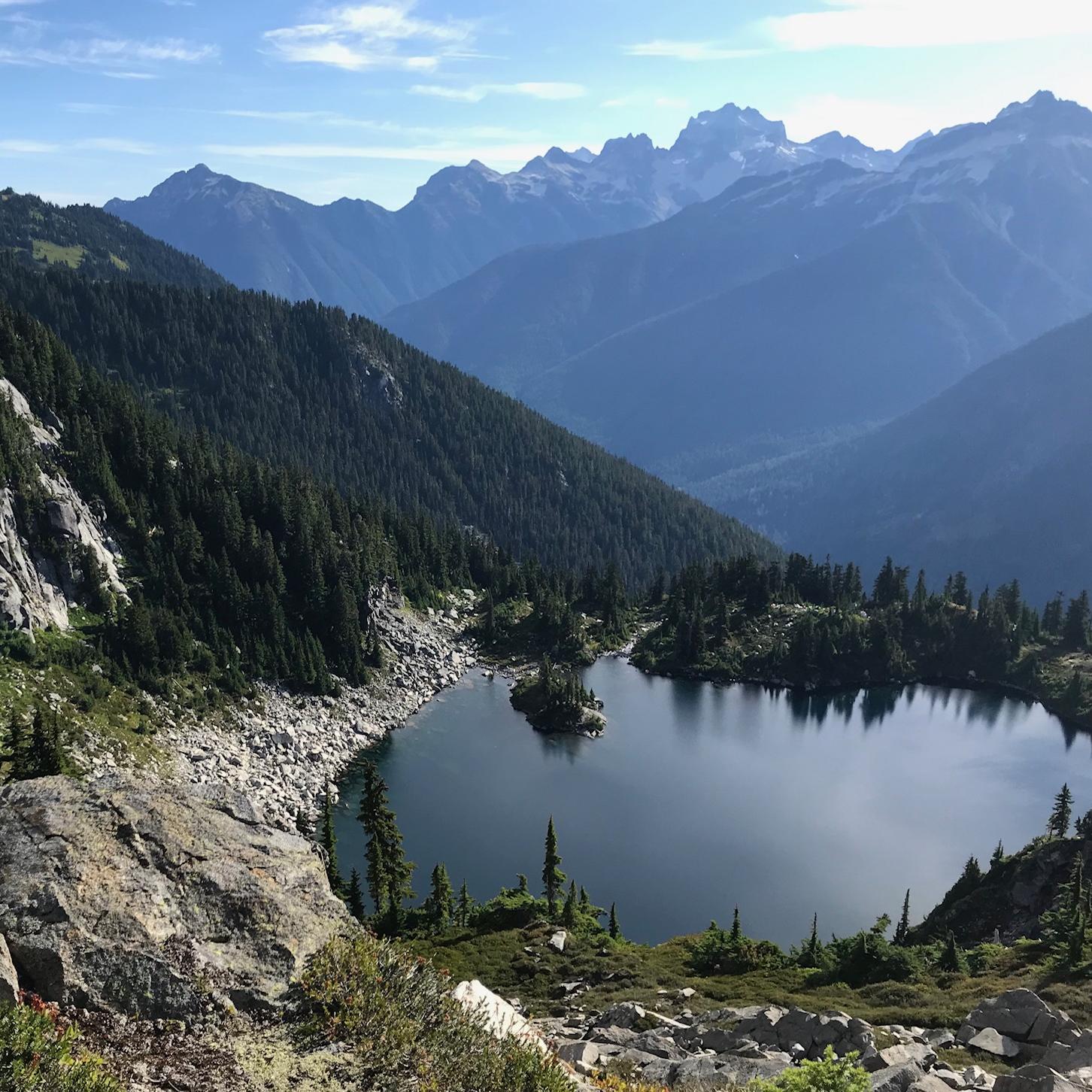 A small subalpine lake with a sea of mountains in the background.