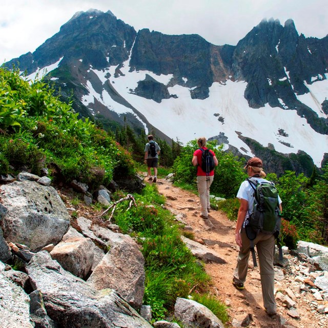 Three hikers travel along a dirt trail in the mountains.