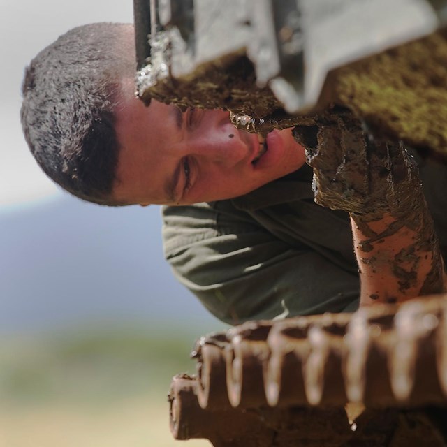 A marine solider scrapes invasive picklweed off an amphibious assault vehicle