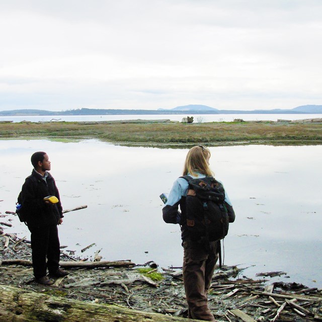 Two scientists with monitoring equipment beside a lagoon.