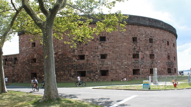 Round fading red brick building with a light blue sky in the background