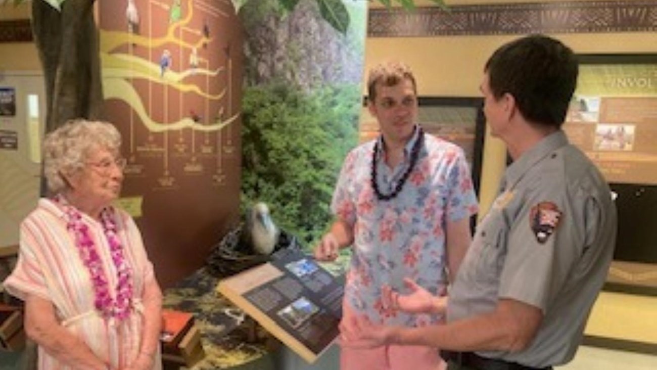 Indoors; park ranger talking to two adults with exhibits in the background.