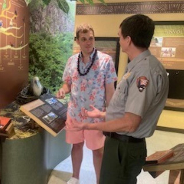 Indoors; park ranger talks to two adults, exhibits in background.