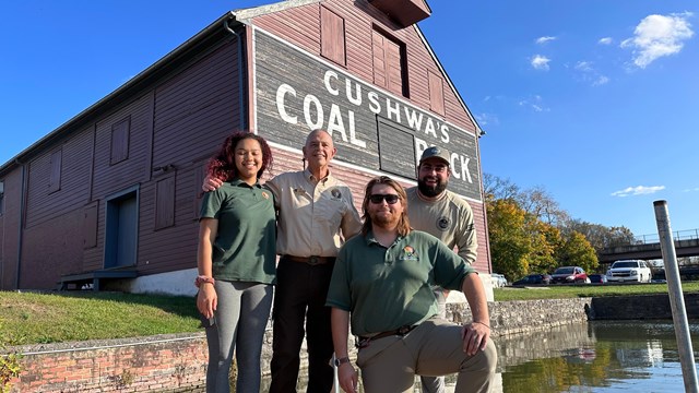 Four volunteers pose for a photo on a dock in front of a wooden building.