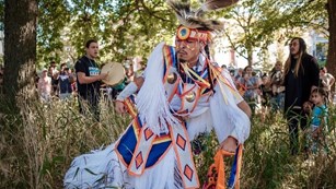 Native American dancer in tall grass with a crowd in the background