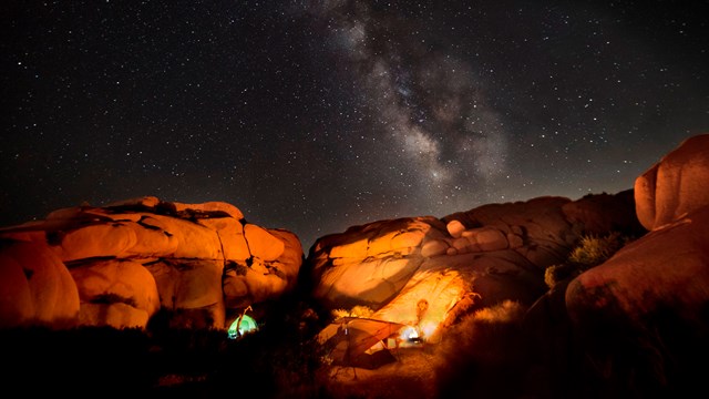 Campsite with tent and campfire in a desert under the Milky Way