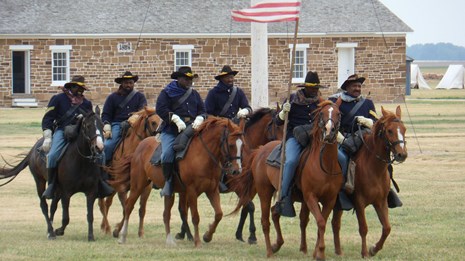 Line of Buffalo Soldier reenactors riding horses at a historic fort