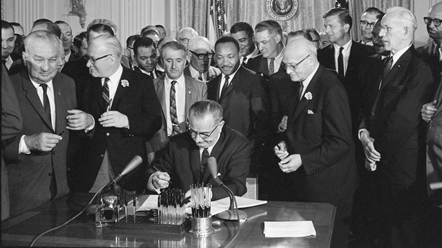 Historic photo of President Lyndon Johnson signing a bill in front of a large crowd
