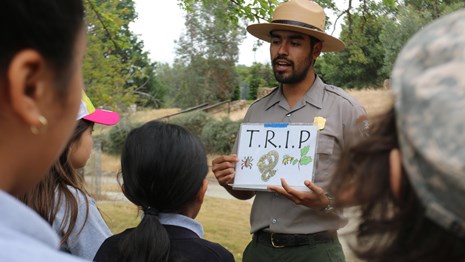 Ranger holding up a sign reading "T.R.I.P" to an audience