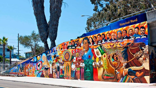 Outside wall decorated by a mural depicting various scenes of Hispanic heritage
