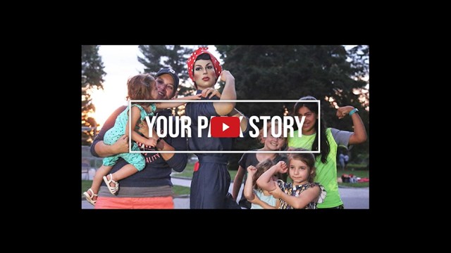 Video screenshot of a group of women and girls standing with a Rosie the Riveter statue