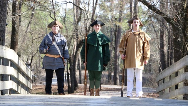 Three young people in Patriots costume stand guard on a bridge.
