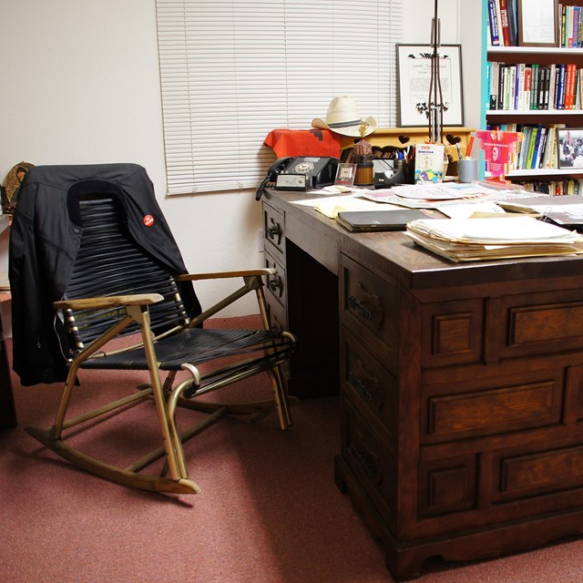 Office desk covered in papers and near a full bookshelf 