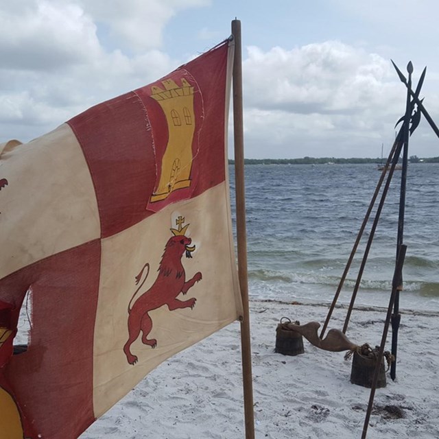 Colonial Spanish flag, shield, and campsite on a beach