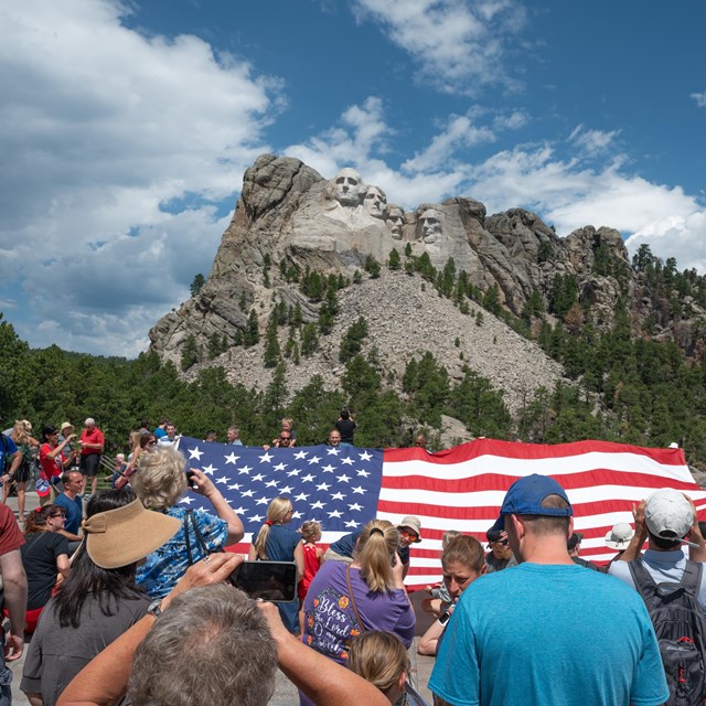 Visitors holding a large U.S. flag in front of Mount Rushmore