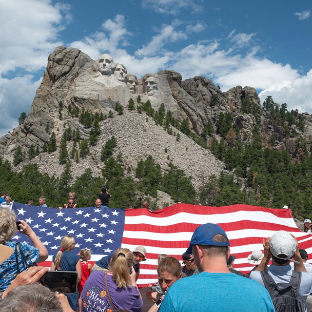 Group of people holding up an enormous American flag in front of Mount Rushmore