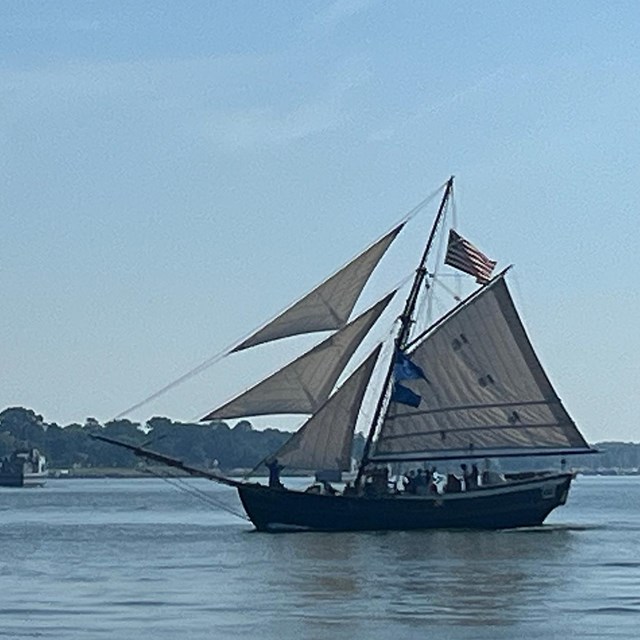Historic-looking sloop with a waving American flag sails across a body of water