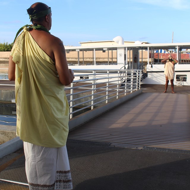 Person in Native Hawaiian clothing standing by a dock leading to a ferry